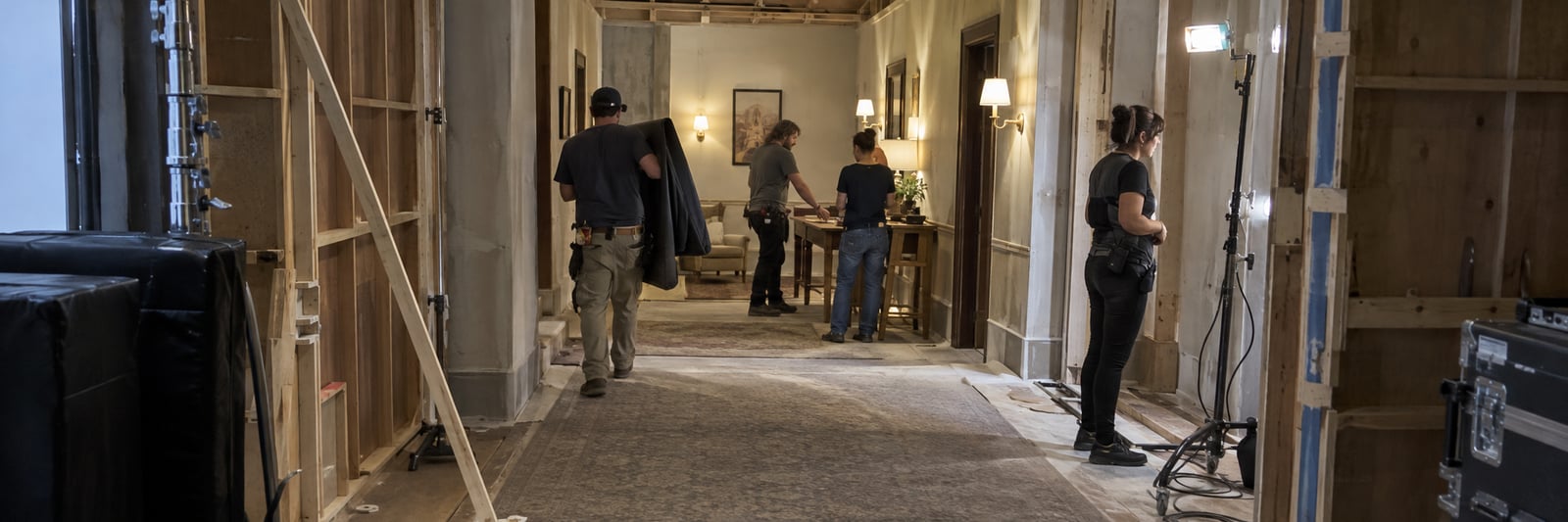 Crew resetting an interior set, with exposed scenery supports, practical lights and equipment.
